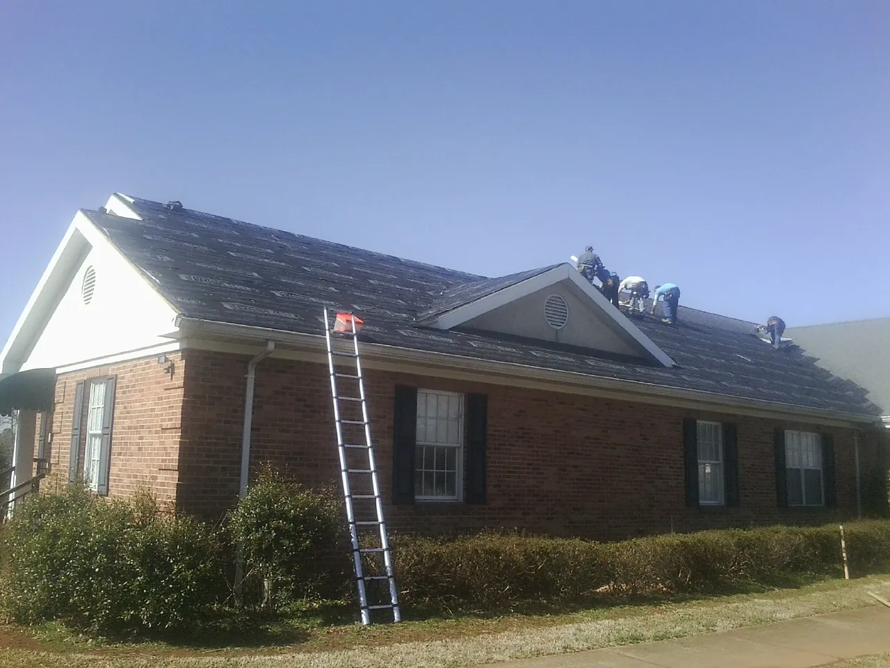 Crew tearing shingles off a brick ranch roof with a ladder set — Emergency Roof Repair work by our crew in Colbert