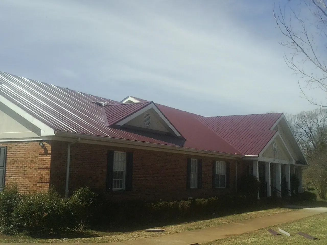 Red metal roof with gabled entries on a long brick building, from a Hail Damage Roof Repair job in Colbert
