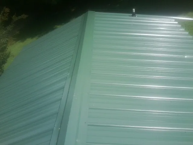 New green metal panels meeting at the ridge of a roof — Flat Roof Repair work by our crew in Colbert