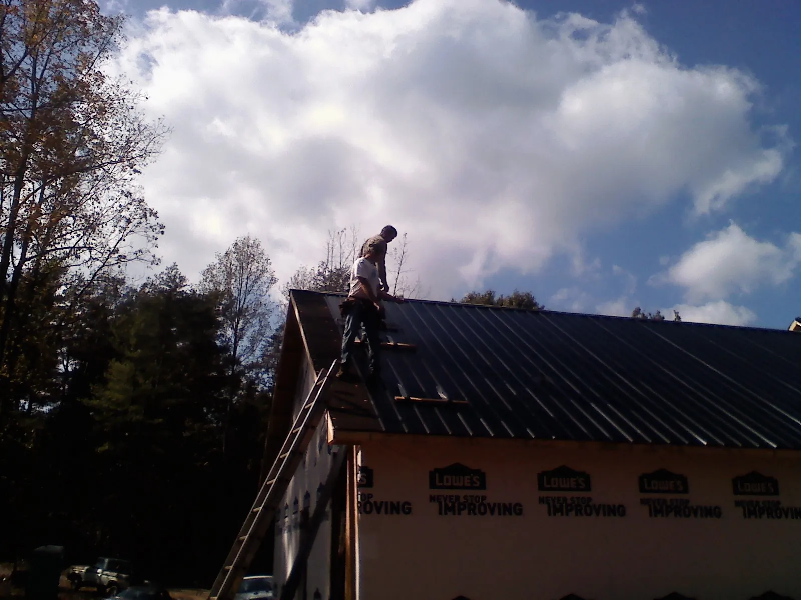 Roofer fastening dark metal panels high against a cloudy sky, from a Roof Inspection job in Colbert